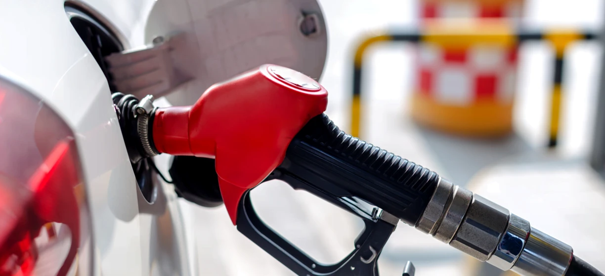 Dystrybutor paliwa na stacji benzynowej z dyszą i wężem, gotowy do tankowania benzyny lub oleju napędowego. Pokazana jest również stacja ładowania pojazdów elektrycznych.