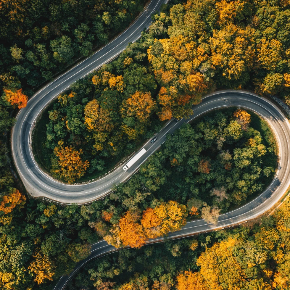 Widok z lotu ptaka na kontrolowaną autostradę wijącą się przez bujny las wiekowy w przełęczy górskiej. Zdjęcie przedstawiające malowniczą leśną drogę.