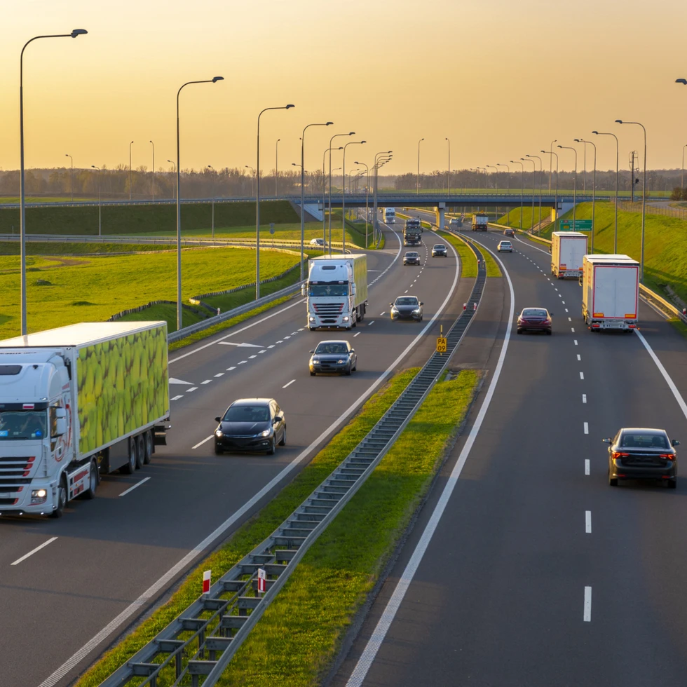 Autostrada wypełniona różnymi rodzajami pojazdów silnikowych, w tym ciężarówkami handlowymi, poruszająca się po gładkiej nawierzchni asfaltowej. Transport i ruch na ruchliwej arterii o kontrolowanym dostępie.